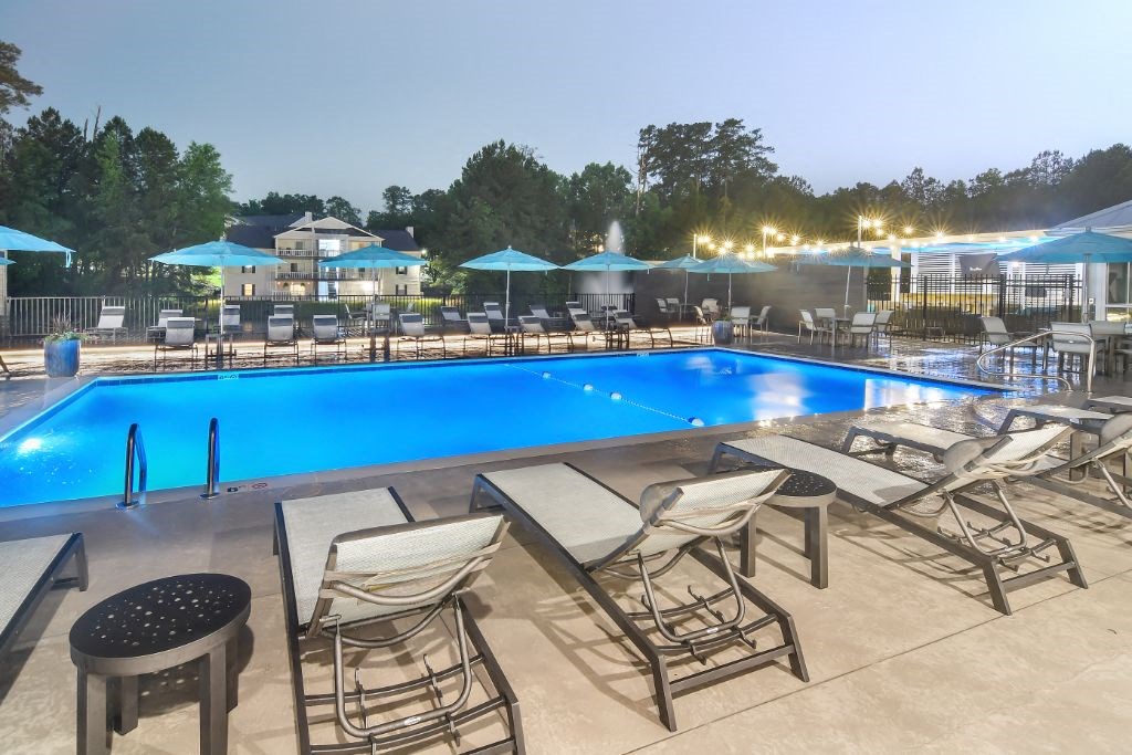 a swimming pool with chaise lounge chairs and umbrellas at night at The Woodlands Apartment Homes, Meridian