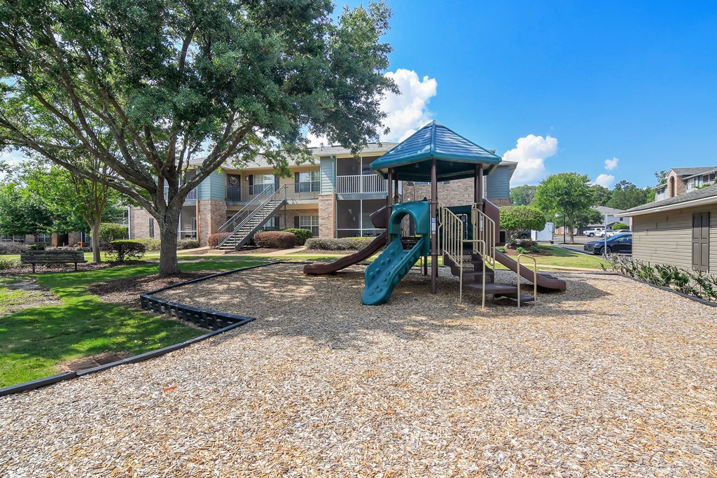 A playground with a slide and a tree in front of a building at Ashford Place Apartment Homes, Flowood, MS
