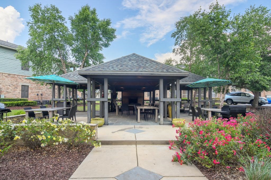 a large pavilion with tables and umbrellas in front of a brick building at Ashford Place Apartment Homes, Flowood