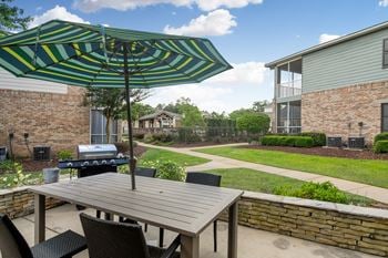 A patio with a table and chairs under a striped umbrella at Ashford Place Apartment Homes, Flowood, MS