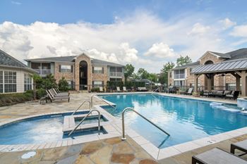 A swimming pool surrounded by a patio with chairs and a building in the background at Ashford Place Apartment Homes, Flowood, Mississippi
