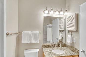 A bathroom with a toilet, sink, and mirror at Ashford Place Apartment Homes, Flowood, MS