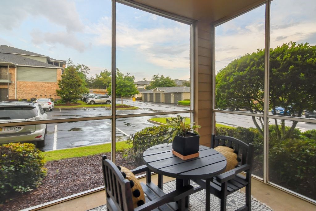 a screened in porch with a small table and chairs and a view of a parking lot at Ashford Place Apartment Homes, Flowood, Mississippi