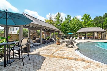 A poolside area with chairs and umbrellas and outdoor fireplace at Legacy Apartment Homes in Ridgeland, MS