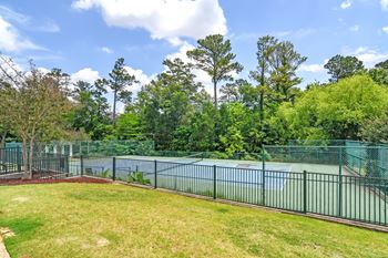 the backyard of a tennis court with a fence and a pond at Legacy Apartment Homes in Ridgeland, MS
