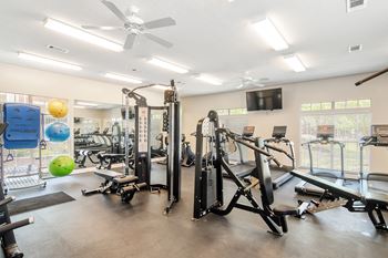 a gym with cardio machines and weights and a tv at Legacy Apartment Homes in Ridgeland, MS