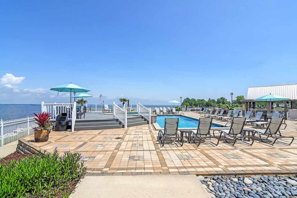 A pool area with chairs and umbrellas overlooking the water at Lakeshore Pointe Apartment Homes, Mississippi, 39047