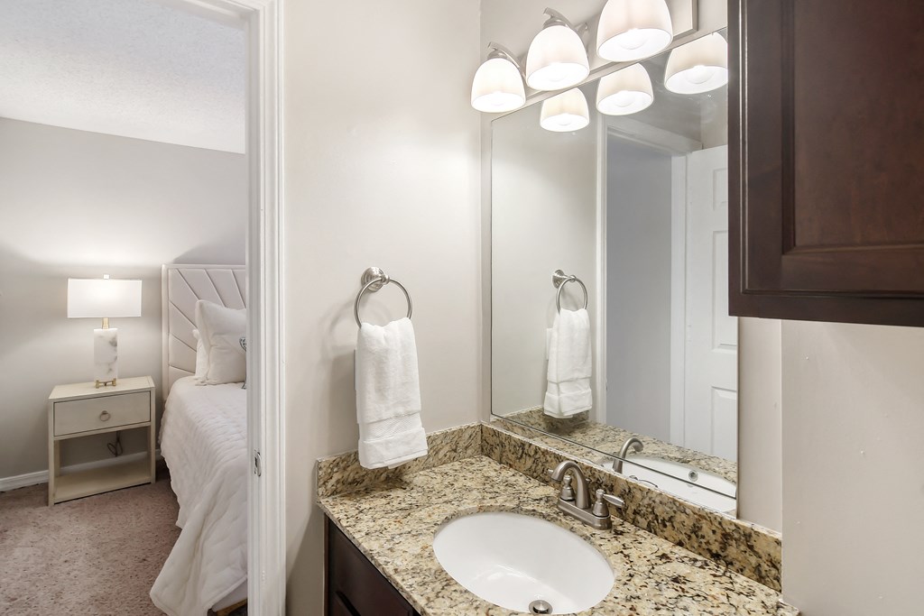 a bathroom with a sink and a mirror and a bed at Lakeshore Pointe Apartment Homes, Brandon, MS