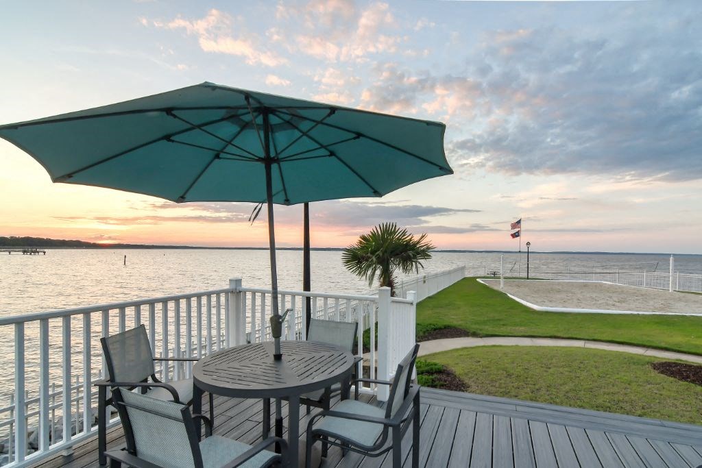 a deck with a table and chairs and an umbrella overlooking a body of water at Lakeshore Pointe Apartment Homes, Brandon, MS, 39047