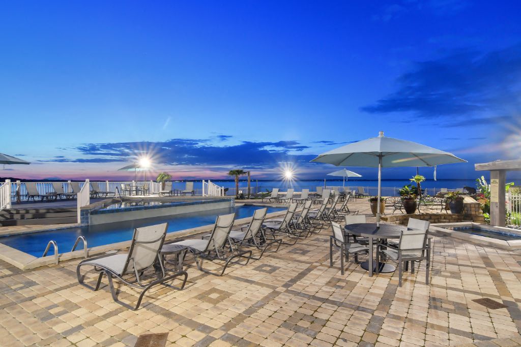 a swimming pool with chairs and umbrellas next to a body of water