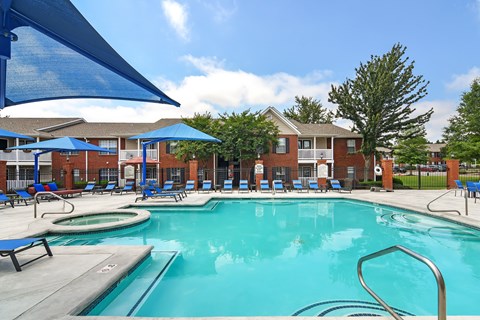 A swimming pool with a blue umbrella and lounge chairs.