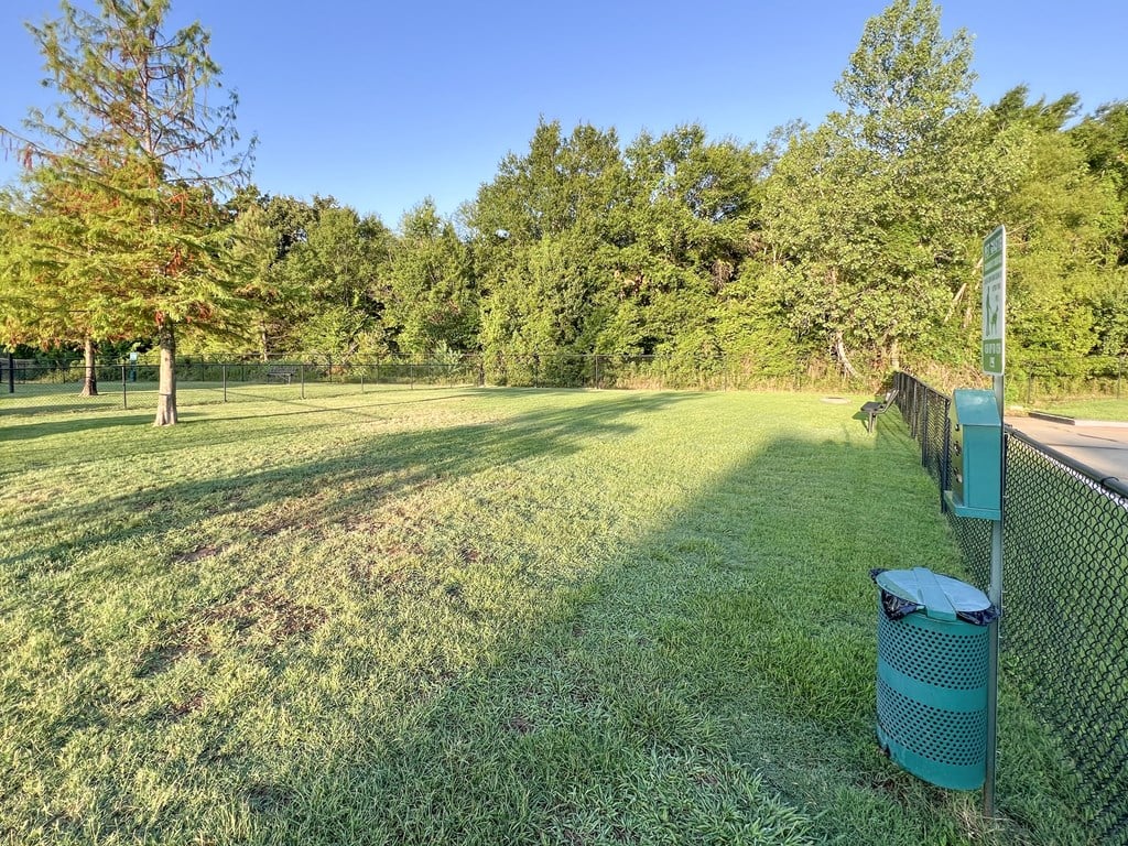 a grassy field with a fence and a trash can at The Madison Apartment Homes in Texas 75703