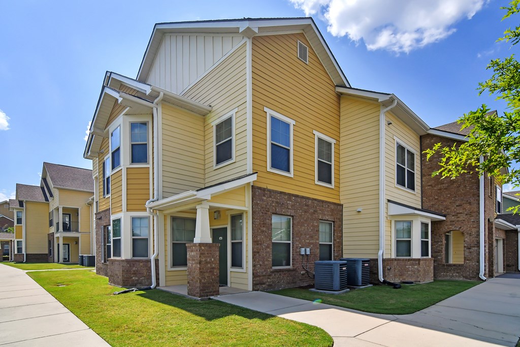 a row of houses with yellow siding and a sidewalk at Audubon Park Apartment Homes, Louisiana