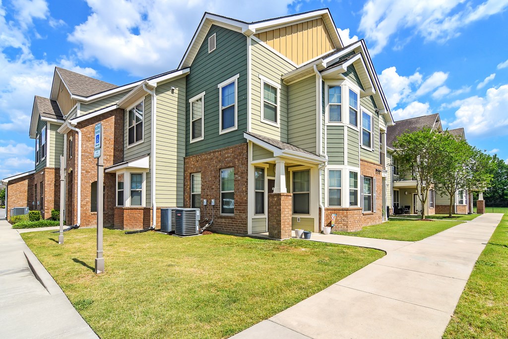 an apartment building with green and brick exterior and a sidewalk at Audubon Park Apartment Homes, Louisiana, 70791
