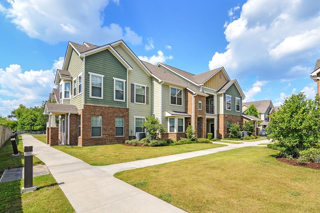 an apartment building with green siding and brick and a sidewalk at Audubon Park Apartment Homes, Louisiana, 70791