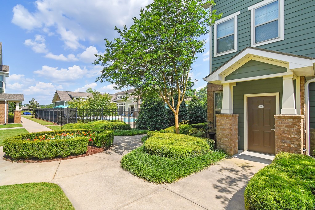 a sidewalk in front of a house with bushes and a tree at Audubon Park Apartment Homes, Louisiana