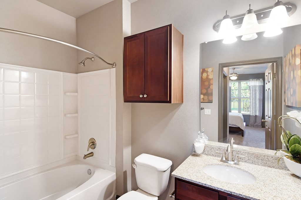 a bathroom with a white tub and a sink and a mirror at Audubon Park Apartment Homes, Louisiana