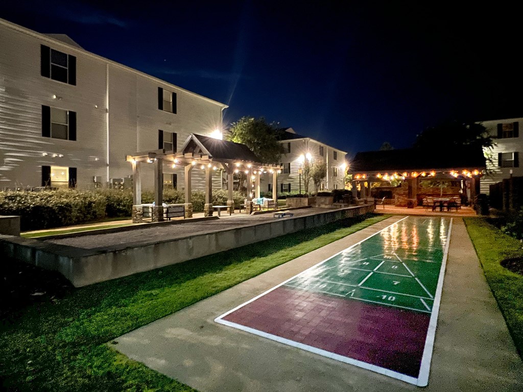 the pool is lit up at night with lights on the buildings at Avalon Apartment Homes, Starkville, MS, 39759