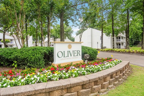 an olivier apartments sign in front of a stone wall and flowers