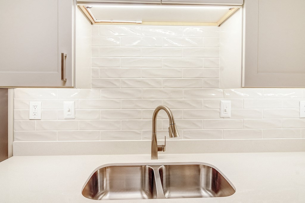 a kitchen sink with a faucet in front of a tiled wall
