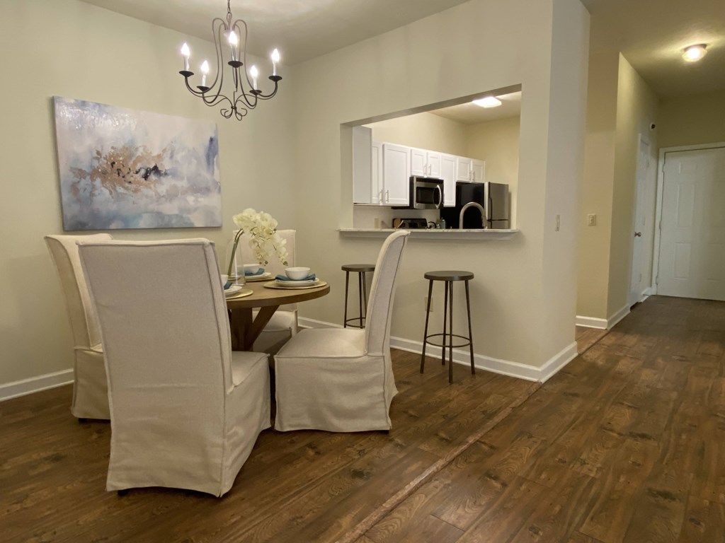 A room with a painting, a chair, a table with a vase of flowers, and a bar area with stools.