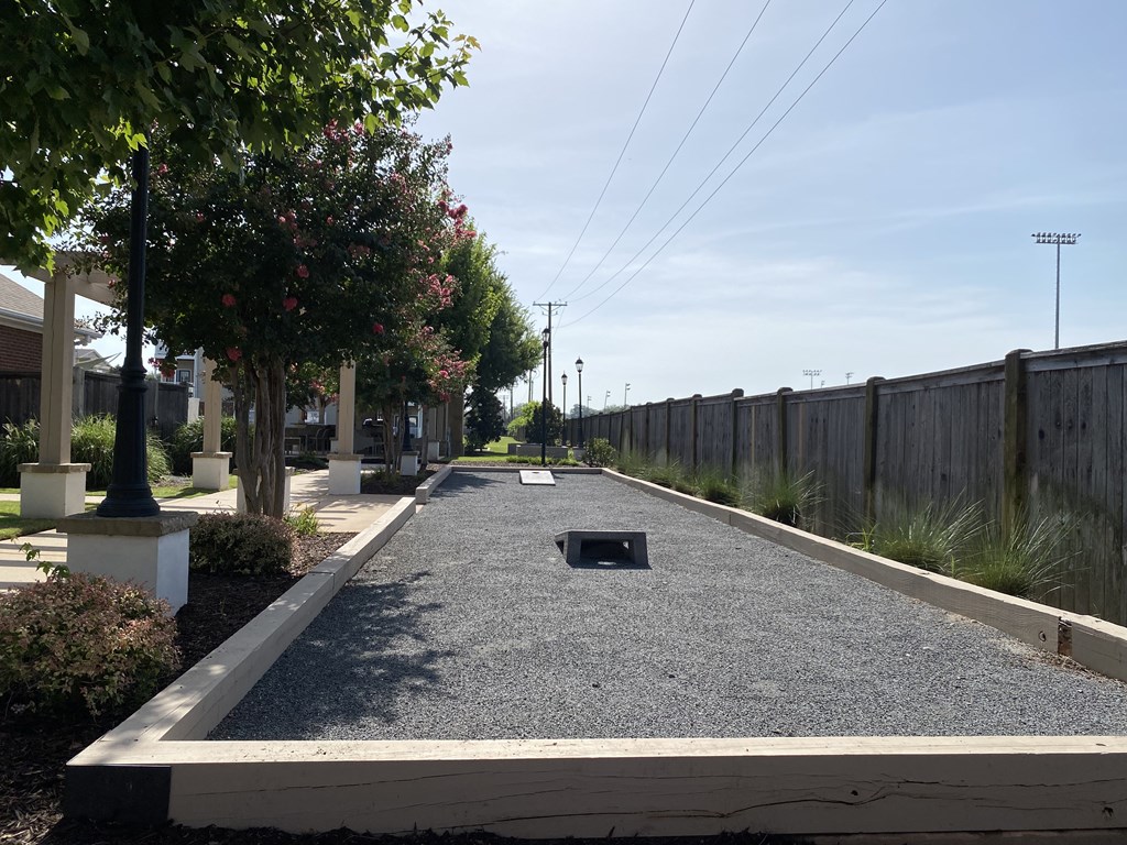 A long, narrow, gravel-covered pathway stretches into the distance between a wooden fence and a row of trees.