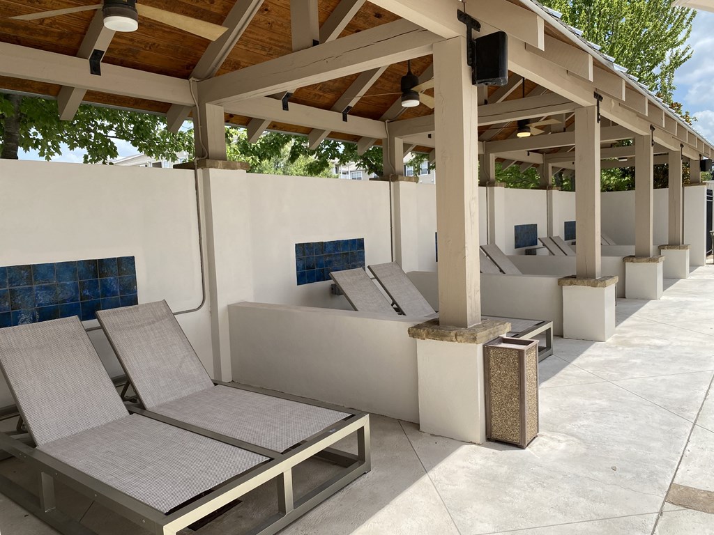 A row of sun loungers are lined up under a wooden roof.