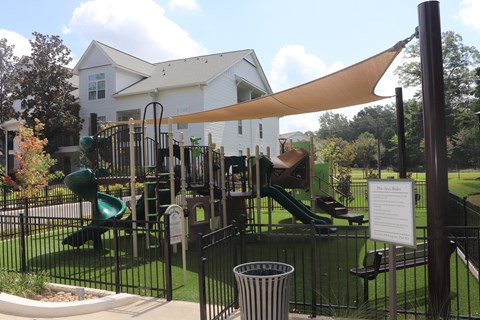 A playground with a green slide and a white house in the background.