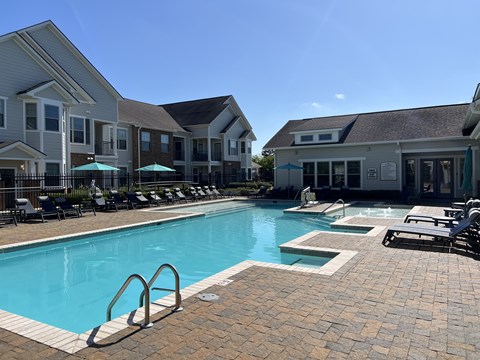 A swimming pool surrounded by lounge chairs and umbrellas in front of apartment buildings.
