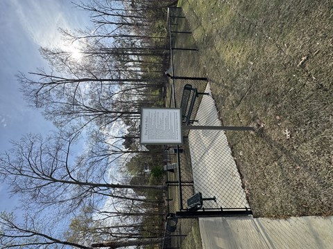 A fence with a sign attached to it is in front of a grassy hill.