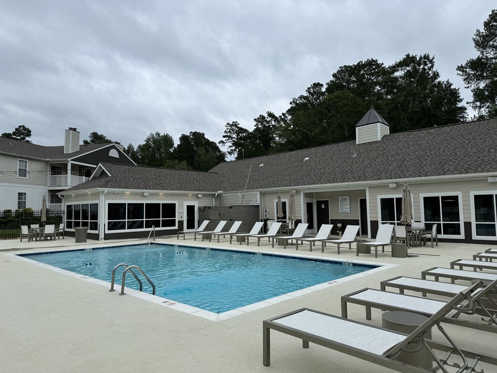 a large swimming pool with lounge chairs in front of a building  at Laurelwood Apartment Homes, Laurel, Mississippi