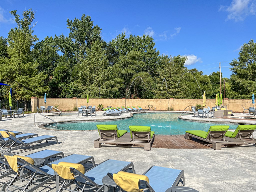 a pool with chairs and tables and a swimming pool with trees at The Madison Apartment Homes in Tyler, TX 75703