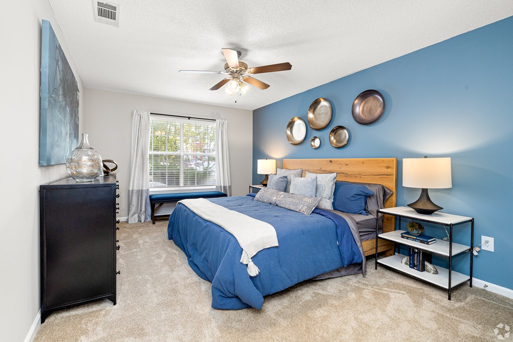 A bedroom with a blue bed and a ceiling fan. at Reserve at Park Place Apartment Homes, Hattiesburg, MS, 39402