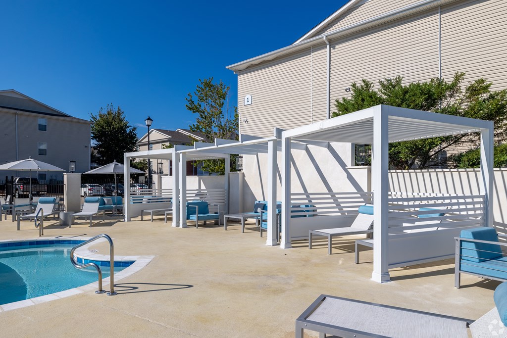 A pool area with sun loungers and a white pergola. at Reserve at Park Place Apartment Homes, Hattiesburg, MS, 39402