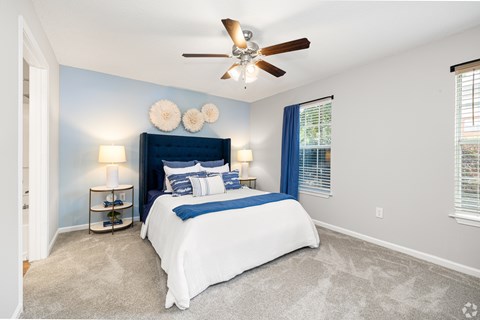 A bedroom with a bed, pillows, a ceiling fan, and a nightstand with a lamp.