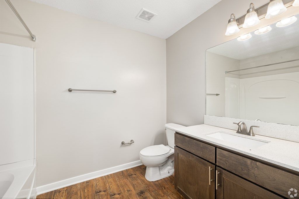 A bathroom with a toilet, sink, and mirror. at Reserve at Park Place Apartment Homes, Hattiesburg