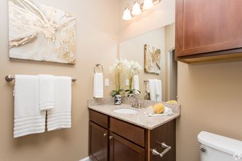 A bathroom with a white tub, brown cabinets, and a painting on the wall at The Retreat Apartment Homes in Williston, ND 