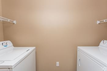 Two white washing machines in a room with beige walls at The Retreat Apartment Homes in Williston, 58801