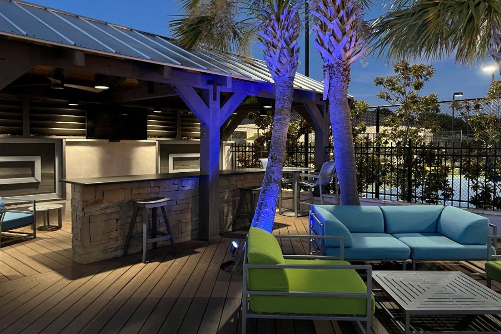a patio with blue couches and a bar and palm trees at Canebrake Apartment Homes, Louisiana