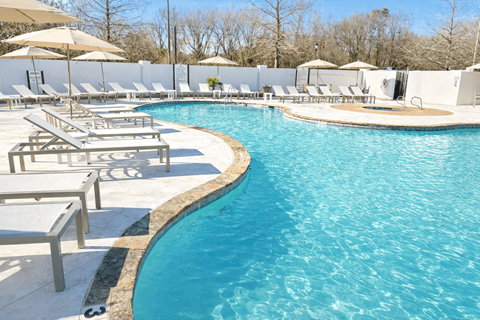 A large swimming pool surrounded by sun loungers and umbrellas.