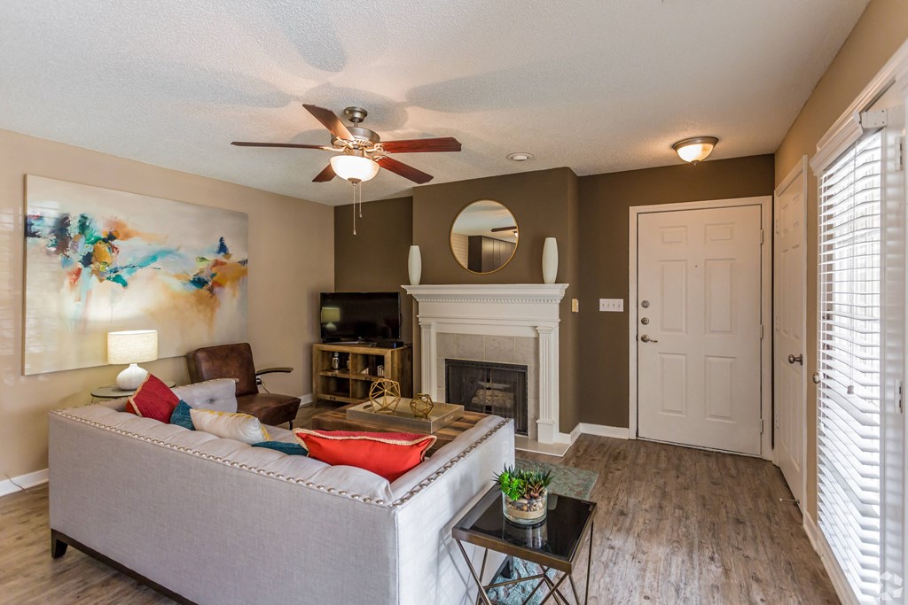 A living room with a grey couch, a fireplace, and a painting on the wall. at Quail Ridge Apartment Homes, Bartlett