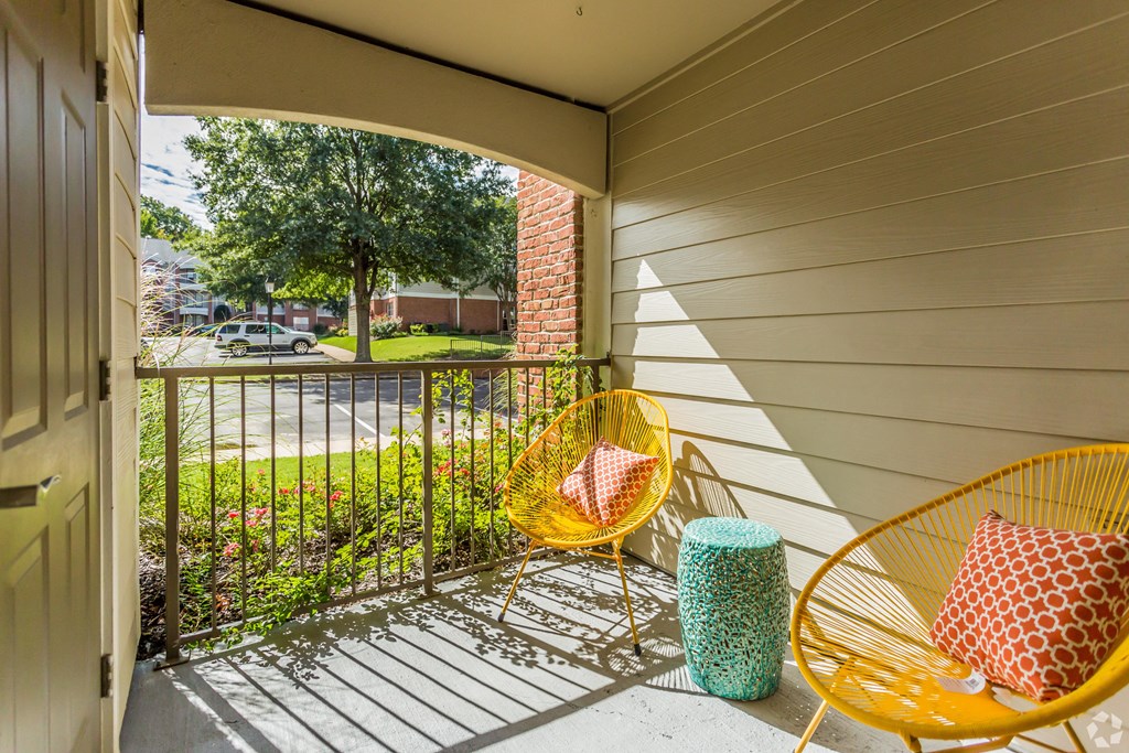 A yellow chair with a red and white pillow is on a porch. at Quail Ridge Apartment Homes, Bartlett
