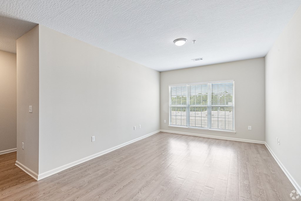 an empty living room with a large window and wood flooring at The Met Apartment Homes, Hattiesburg