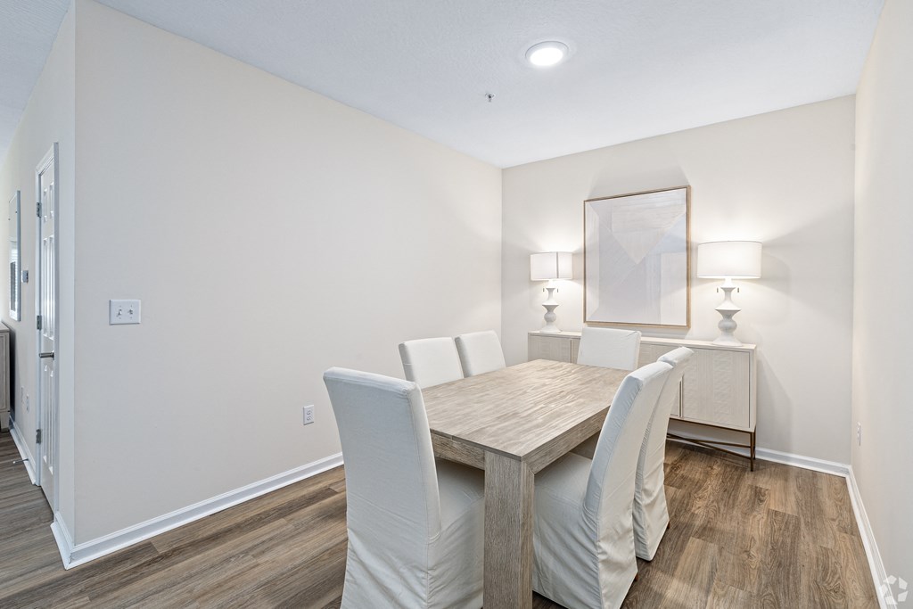 a dining room with a wooden table and white chairs at The Met Apartment Homes, Hattiesburg