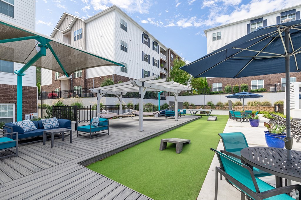 a patio with blue chairs and umbrellas and a green turf at The Met Apartment Homes, Hattiesburg, Mississippi
