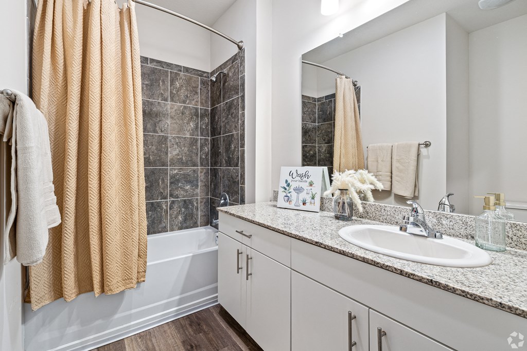 a bathroom with a sink and a shower and a mirror at The Met Apartment Homes, Hattiesburg, 39402
