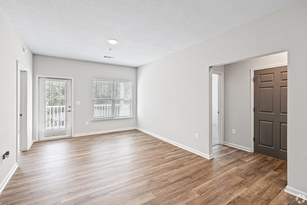 an empty living room with wood flooring and a brown door at The Met Apartment Homes, Mississippi 39402