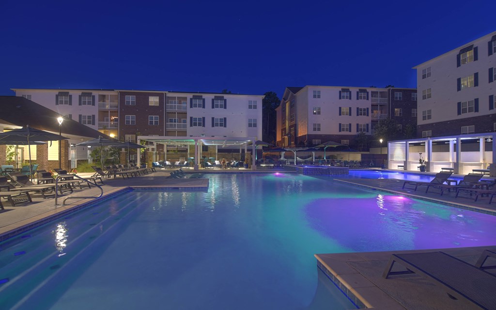 A large swimming pool lit up with blue and purple lights at night at The Met Apartment Homes, Hattiesburg, MS
