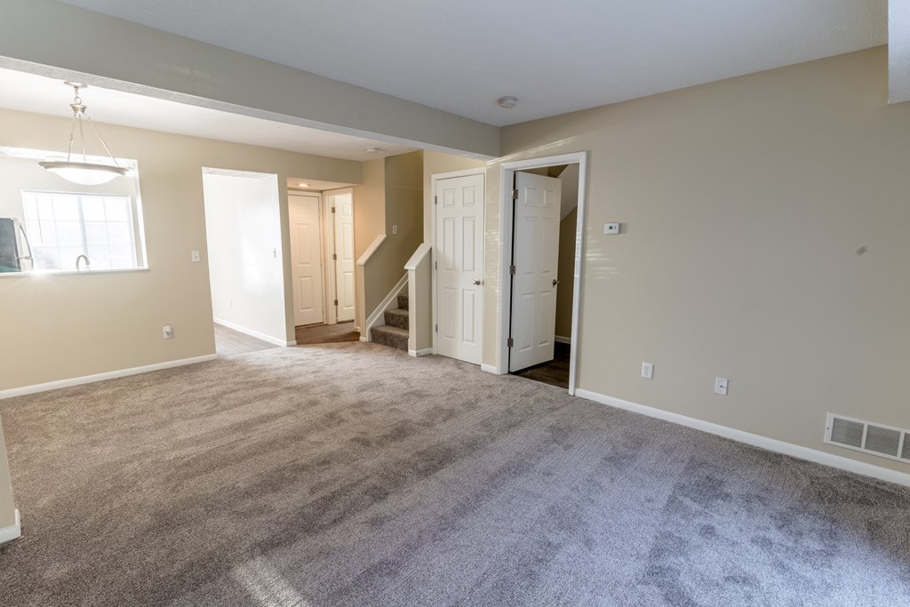 an empty living room with carpeting and a door to a staircase
