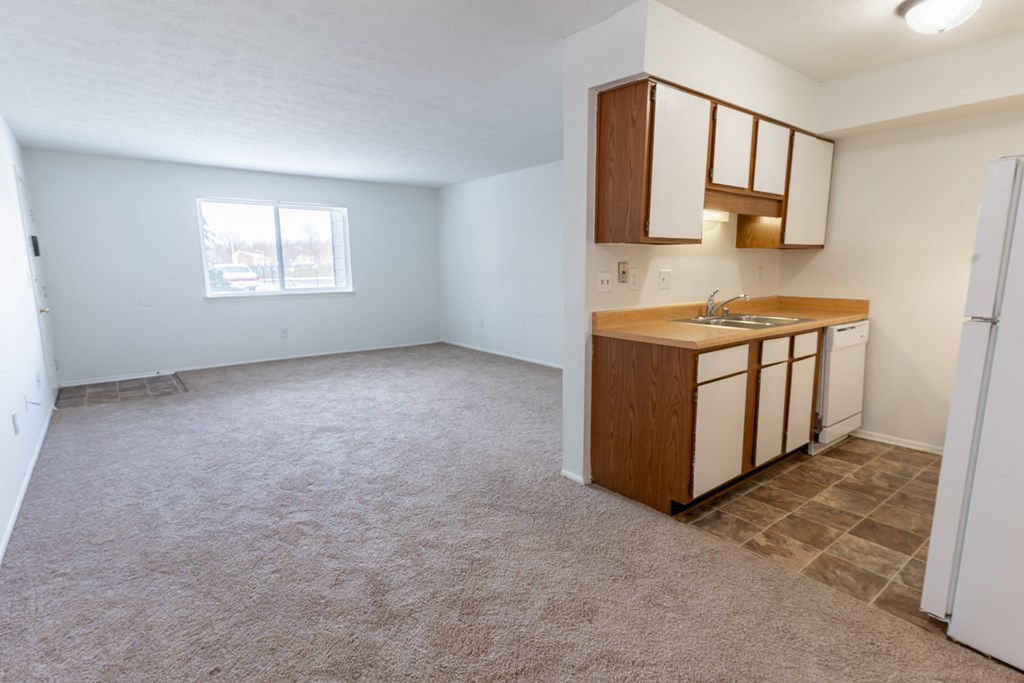 an empty living room with a kitchen in the background